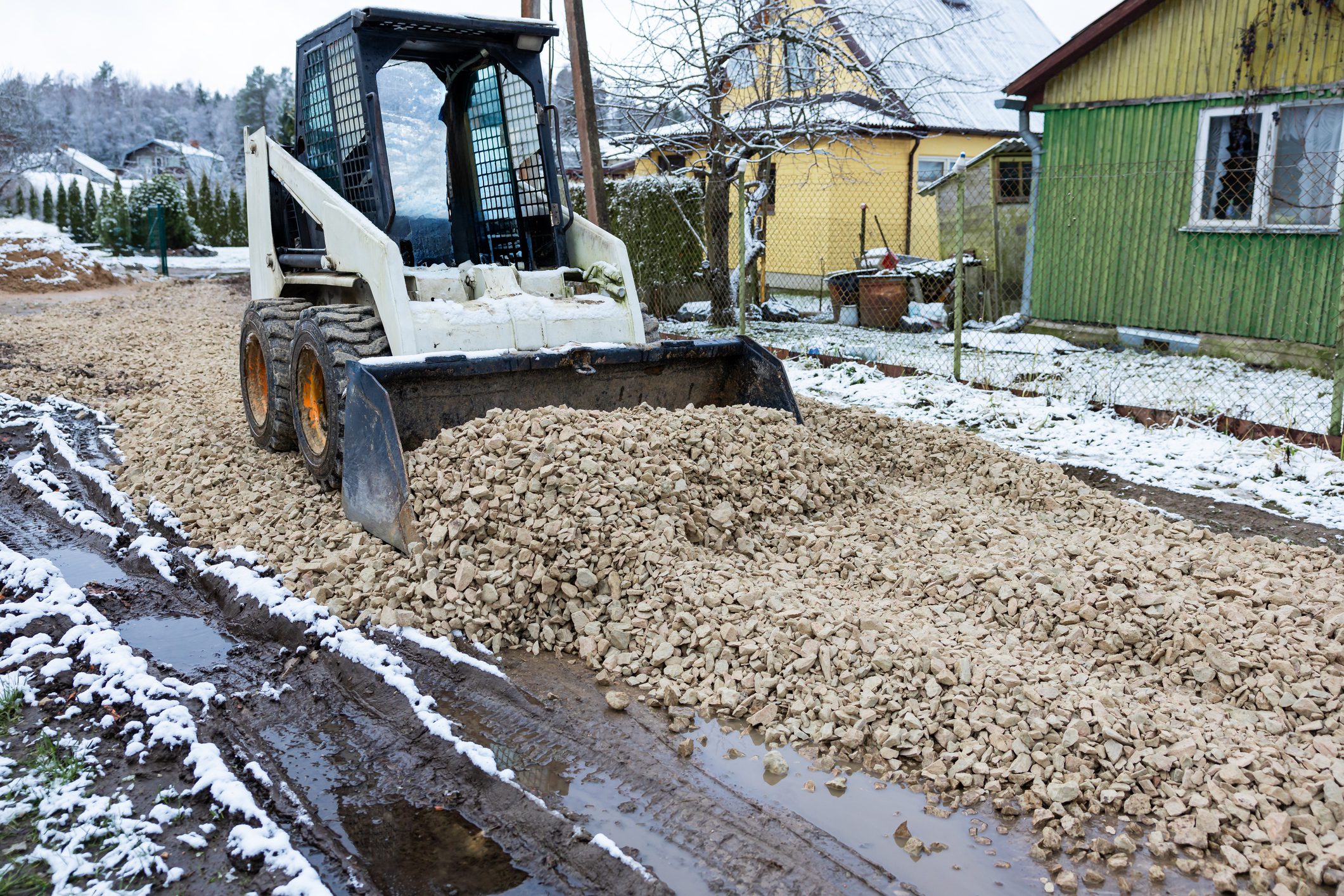 Skid steer loader spreading gravel on road.